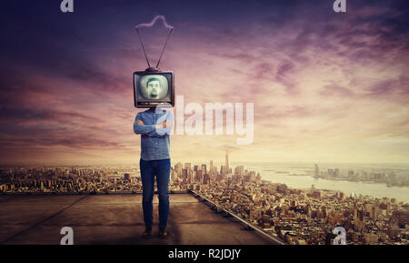 Addicted man with crossed arms and old tv instead of head standing on skyscraper rooftop over big city sunset horizon. Television manipulation and bra Stock Photo