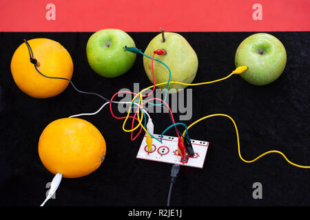 Cables connected to a device and to apples, oranges and pears on display Stock Photo
