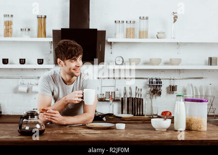 happy young man drinking coffee at table with toasts and coffee pot in kitchen at home Stock Photo