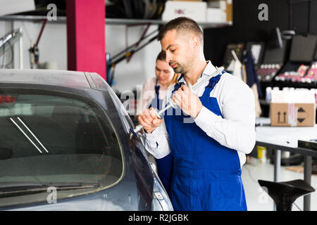 Concentrated mechanic performing car body repair at auto workshop with tools for repairing dents Stock Photo