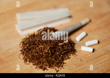 Hand rolling tobacco, paper and filters to make cigarettes on rustic wood Stock Photo