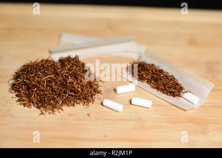 Hand rolling tobacco, paper and filters to make cigarettes on rustic wood Stock Photo