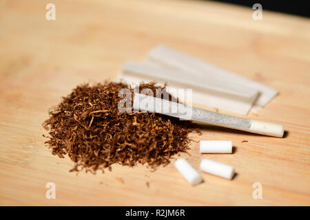 Hand rolling tobacco, paper and filters to make cigarettes on rustic wood Stock Photo