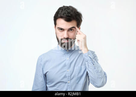 Let me think. Serious hispanic man with beard, keeps index finger on temple, recollect something in mind Stock Photo