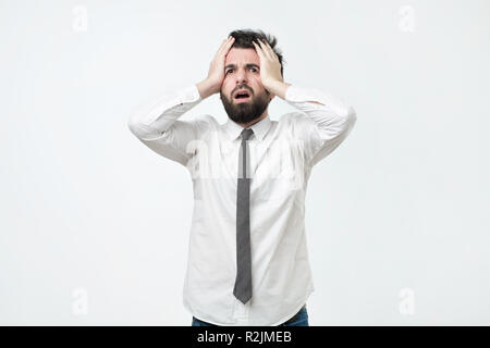 Desperate, stressed young european man looking at camera in terror and shock, holding head Stock Photo