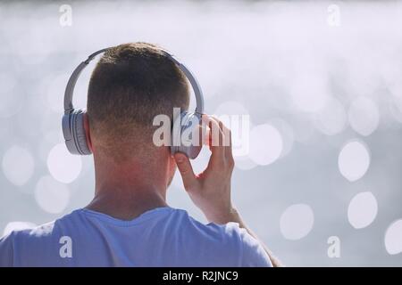 Young man with headphones listening music against bokeh of waves of sea. Stock Photo