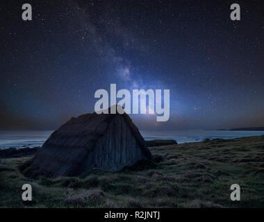Stunning vibrant Milky Way composite image over landscape of seaweed drying hut at Freshwater West beach in Wales Stock Photo