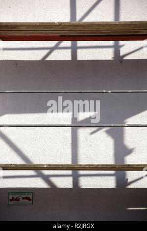 Scaffolding pipes and wooden inlays cast abstract shadows on a wall Stock Photo