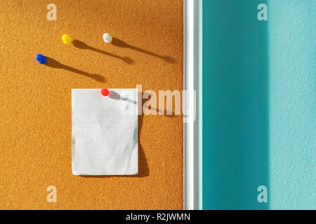 Orange Cork board with one paper note pinned and several different color pins above with shadows from the side sunlight through the window, empty spac Stock Photo