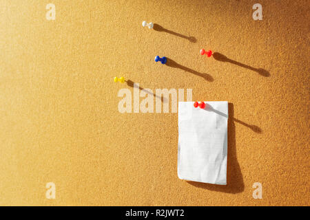 Orange Cork board with one bulletin paper note pinned and several different color pins above. Warm sunlight from the side Stock Photo