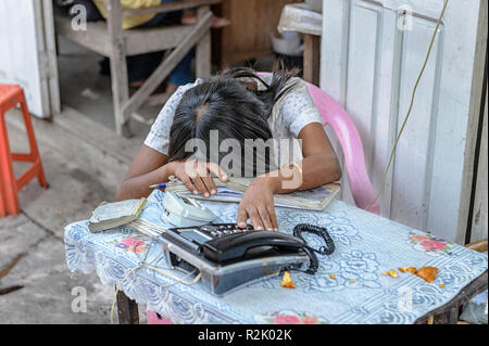 Woman phone vendor asleep or napping at work at a local call stand in Mandalay, Myanmar (Burma) Stock Photo