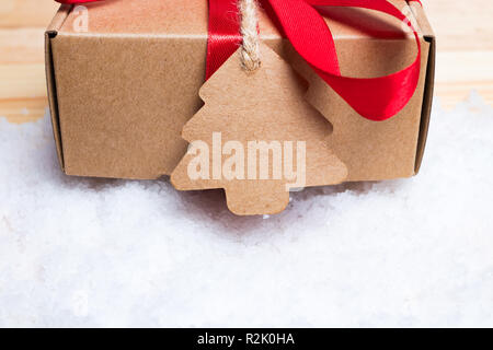 Christmas gift or present on white snow. Red ribbon bow. Label with twine. Stock Photo