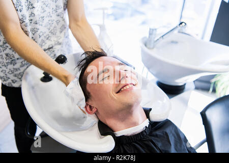 Man hairdresser wiping head of a handsome smiling client with a towel at the barbershop. Stock Photo