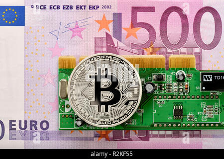 Symbolic image of digital currency, silver physical coin Bitcoin on 500 EURO banknote and circuit board Stock Photo