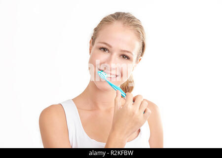 Studio shot of beautiful young woman brushing her teeth while looking at camera and smiling. Isolated on white background. Stock Photo