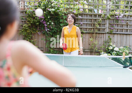 Mother and daughter playing table tennis in sunny backyard Stock Photo