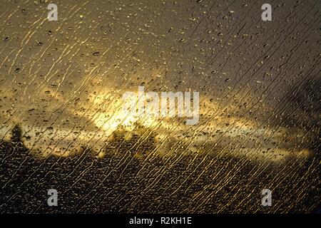 Close up of raindrops on window with a stormy sunset in the background Stock Photo