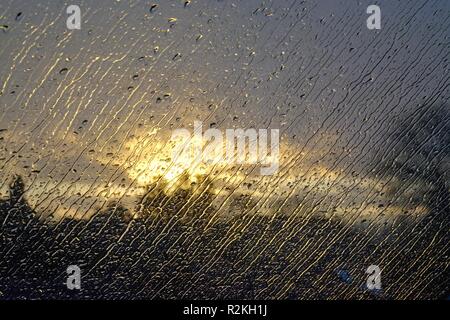 Close up of raindrops on window with a stormy sunset in the background Stock Photo