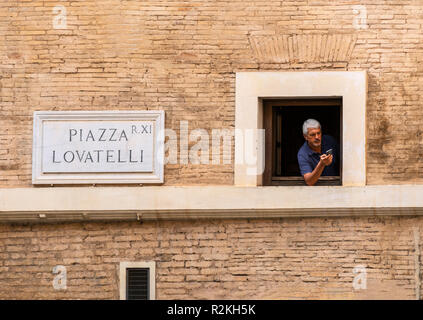Man looking for phone signal from a window, in the Piazza Lovatelli, rione XI - Sant'Angelo,  Rome, Italy Stock Photo