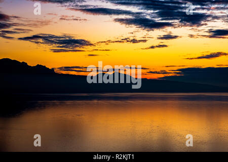 Beautiful colorful sunset in autumn with silhouettes of the French Alps and fantastic orange glowing reflected colors on the Lake Geneva, Switzerland. Stock Photo