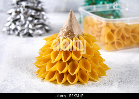 How to make a Christmas tree from raw pasta conchiglie. The process of making Christmas trees from pasta, cardboard plates, hot glue and paint or spra Stock Photo