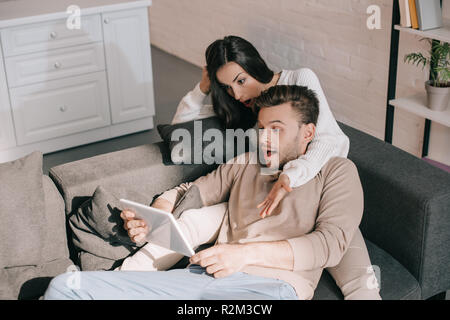 shocked young couple using tablet together on couch at home Stock Photo