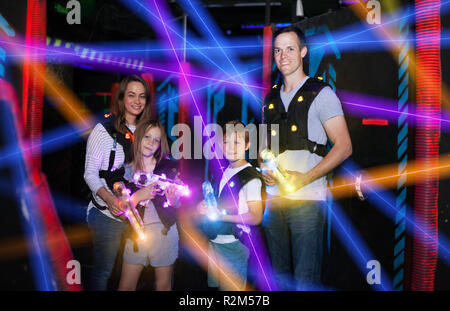 Group of happy kids and adults having fun on dark lasertag arena in colorful beams of laser guns Stock Photo