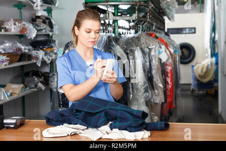 Focused diligent friendly  girl worker of laundry writing receipt while taking clothes for dry cleaning Stock Photo