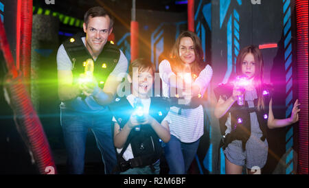 Group of happy kids and adults having fun on dark lasertag arena in colorful beams of laser guns Stock Photo