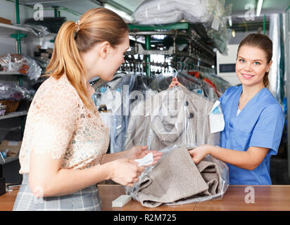 Young diligent positive woman working with client in modern laundry, returning clothing after dry cleaning Stock Photo