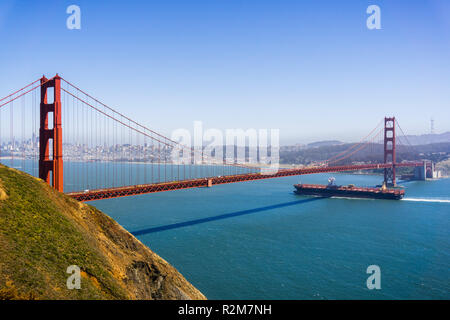 Cargo ship passing under Golden Gate Bridge on a sunny day; San Francisco skyline in the background; California Stock Photo