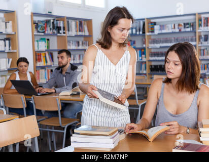 Young female student sitting in university library, working with her teacher Stock Photo