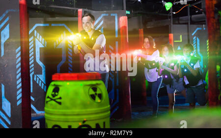 Group of happy kids and adults having fun on dark lasertag arena in colorful beams of laser guns Stock Photo