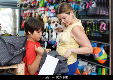 Smiling teen boy with mother choosing bag dog carrier for their puppy in pet supplies store Stock Photo