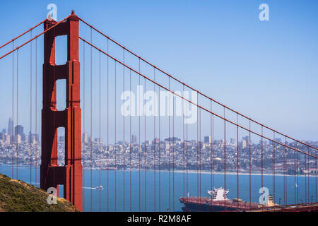 The north tower of Golden Gate Bridge; San Francisco's skyline visible in the background; large cargo ship passing under the bridge; Stock Photo