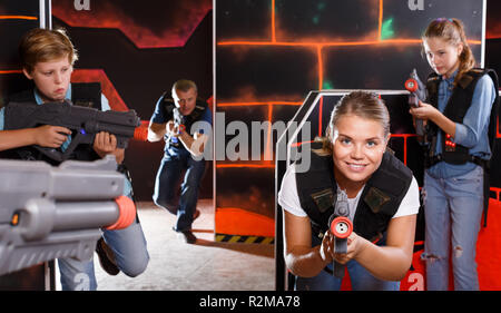 Foto Stock Excited boy aiming laser gun at other players during laser tag  game in dark room