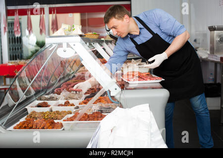 Professional butcher arranging meat products in display case of butcher shop Stock Photo