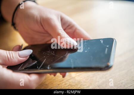 Close view of woman's hands with a black mobile phone whose screen is broken. Stock Photo