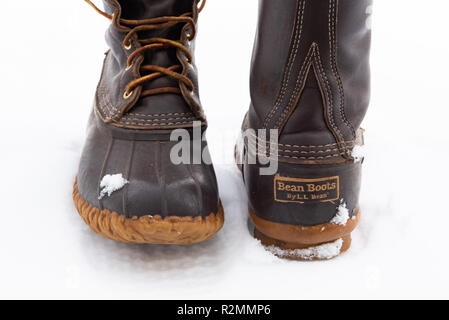A pair of worn LL Bean boots in the snow, showing the leather and rubber construction and the distinctive chain link tread design and waterproof sole. Stock Photo