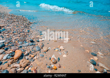 Pebble stones on the shore close up in the blurry sunset light in the distance background. Stock Photo