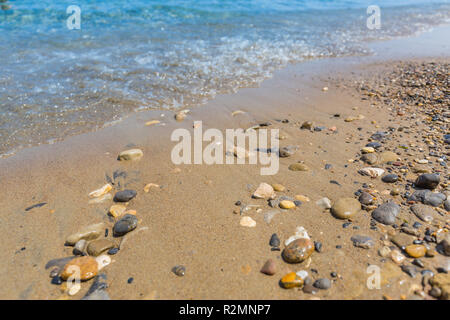 Pebble stones on the shore close up in the blurry sunset light in the distance background. Stock Photo