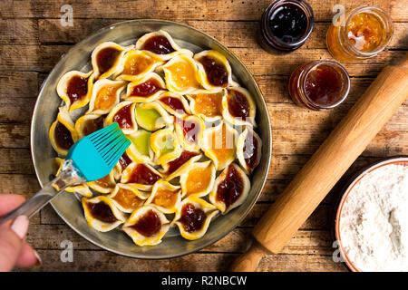 Adding egg yolk to homemade sweet pie with various fruit jams Stock Photo