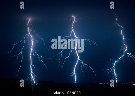 Three branched lightning bolts next to each other strike down to earth from a severe summer thunderstorm in The Netherlands Stock Photo