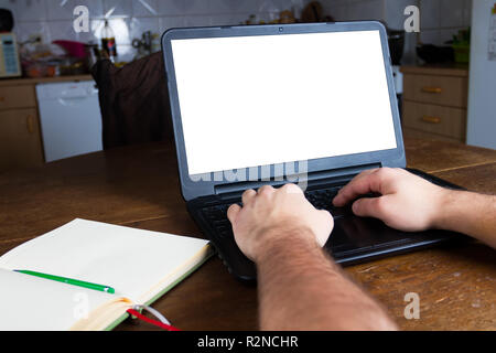 Man typing on a laptop computer in vintage kitchen. Blank white screen ready for mockup. Notepad. Old retro scratched wooden table. Stock Photo