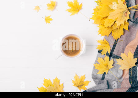 Flat lay cup of coffee among side composition of autumn leaves and checkered scarf on white wooden table, top view with copy space. Stock Photo