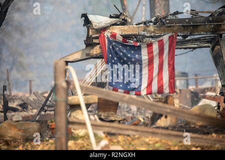 A U.S. flag hangs from a burned out home in the Skyway Villa Mobile Home and RV Park destroyed in the massive Camp Fire November 17, 2018 in Paradise, California. Stock Photo