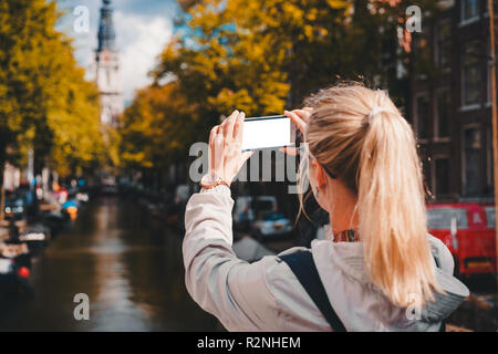 Woman tourist taking a picture of canal in Amsterdam on the mobile phone. Warm gold afternoon sunlight. Travel in Europe Stock Photo