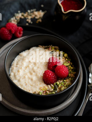 Porridge in dark bowl with fresh raspberries and coulis in jar Stock Photo