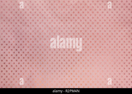 Rose gold background from metal foil paper with a pattern of sparkling stars closeup. Texture of pink metallized wrapping holiday paper surface. Stock Photo