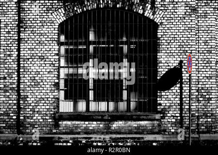 Closed industrial estate, 'No stopping' sign casting shadow on brick wall of old factory building, barred windows Stock Photo